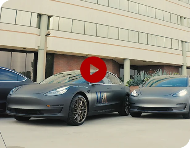 Two matte black Tesla vehicles branded with Michael Burgis & Associates in front of modern office building for workers' compensation mobile services
