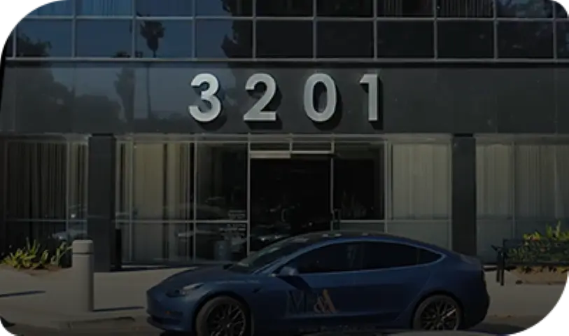 Blue Tesla featuring Michael Burgis & Associates logo parked in front of modern office entrance at 3201 for California workers' compensation consultations