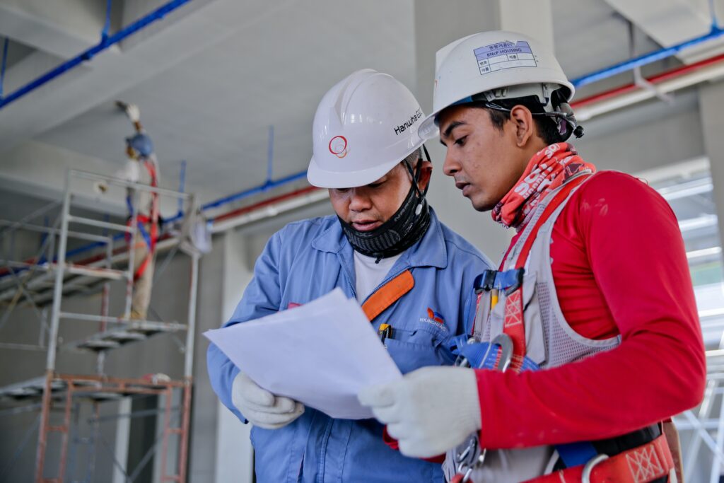 Two construction workers in hard hats and safety gear examining plans illustrating workplace injuries requiring workers compensation attorney in Sherman Oaks California