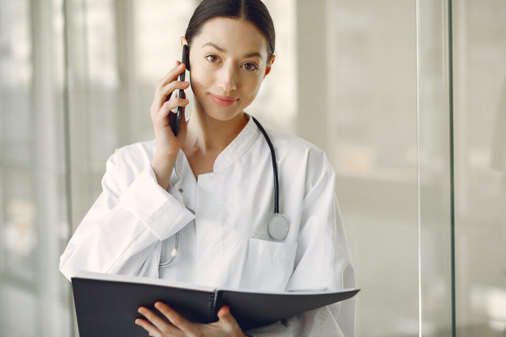 Female doctor with stethoscope holding clipboard and talking on phone coordinating medical treatment for workers compensation cases in Pomona California