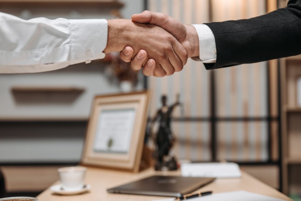 Business professionals shaking hands across desk with Lady Justice statue symbolizing successful workers compensation claim resolution in Sherman Oaks California