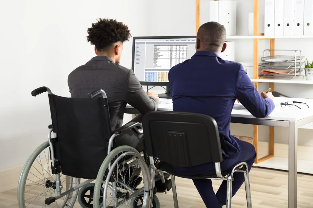 Business professional in wheelchair working at desk with colleague illustrating disability discrimination and accommodations in Sherman Oaks employment law