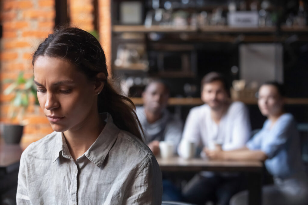 Young woman looking concerned while colleagues talk in background representing workplace harassment and discrimination claims in Sherman Oaks California