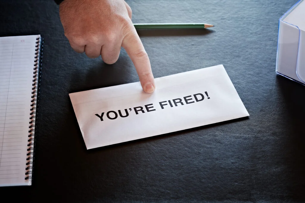 Hand pointing to envelope labeled YOU'RE FIRED on desk highlighting wrongful termination cases handled by employment law attorneys in Sherman Oaks California
